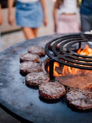 Burgerpatties auf einer Grillplatte, in der Mitte brennt ein Feuer.