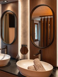 Zwei Waschbecken mit je einem ovalen Spiegel darüber, in einem liegen zwei Handtücher.