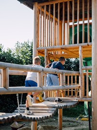 Zwei Kinder laufen über eine Brücke zum Kletterturm am Spielplatz.