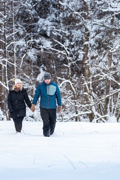 Ein Paar spaziert im Schnee, hinter ihnen ein schneebedeckter Wald.