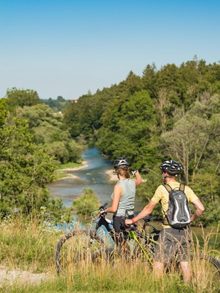 Zwei Radfahrer stehen neben ihren Rädern auf einem Pfad und betrachten den nahegelegenen Fluss.