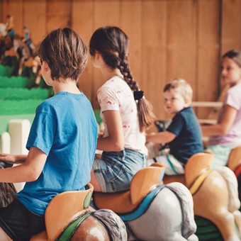 Kinder sitzen auf Pony-Figuren in einer Reihe.