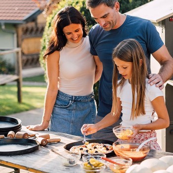 Ein Kind belegt eine Pizza, die Eltern schauen dabei zu.
