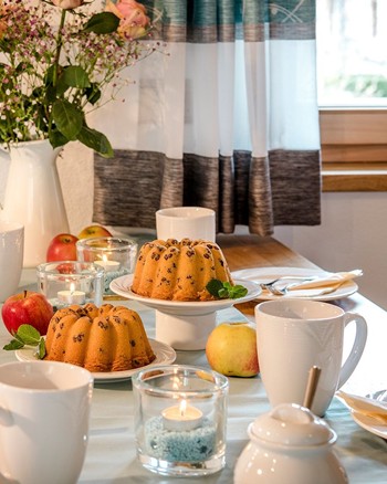 Esstisch mit zwei Gugelhupfen und Äpfeln zur Dekoration.