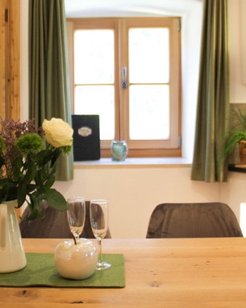 Vase mit gemischten Blumen, Apfel-Figur und Sekt-Gläser auf einem Tisch.