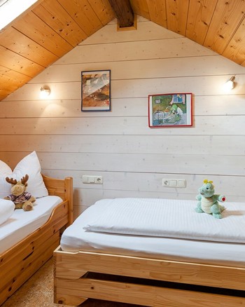 Zwei Einzelbetten mit Stofftieren darauf in einem Zimmer im Dachgeschoss.