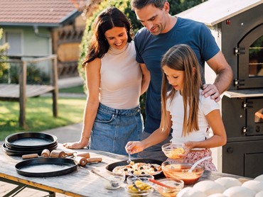 Ein Kind belegt eine Pizza, die Eltern schauen dabei zu.