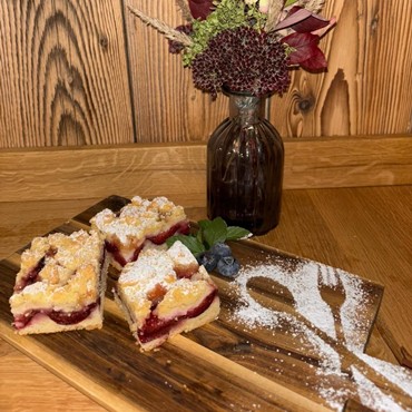 Pflaumen-Streusel-Kuchen auf einem Holzbrett mit Puderzucker-Dekoration.