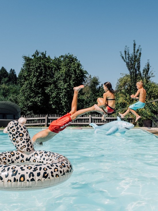 Drei Kinder springen vom Beckenrand in den Pool.