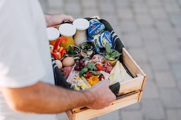 Die Frühstücksbox mit Käse, Wurst, Gemüse, Eiern, Joghurt und Säften wird von einem Mann getragen.