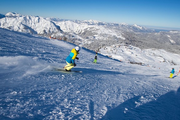 Skifahrer fahren die Piste hinunter, der Blick geht weit in die schneebedeckte Landschaft.