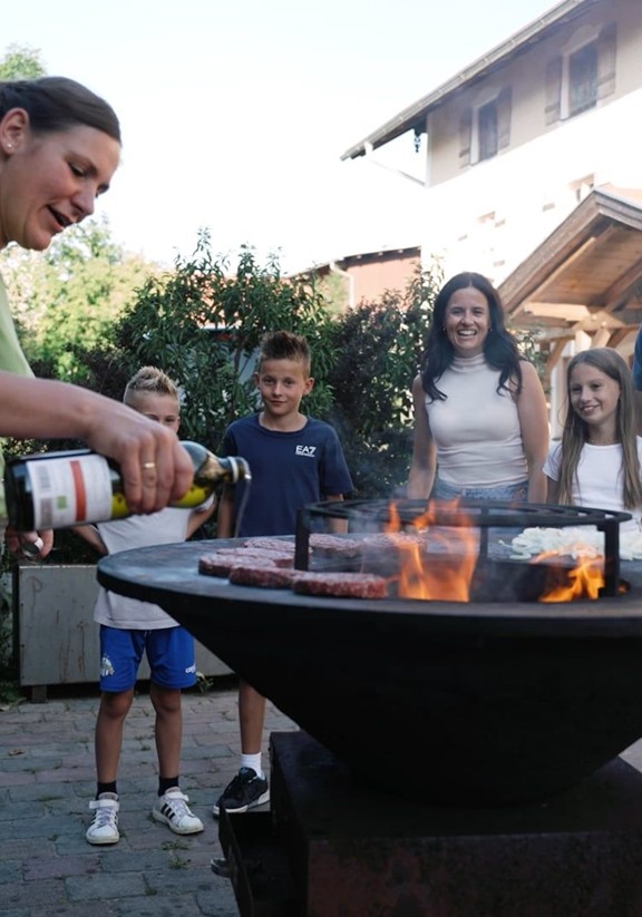 Eine Familie steht um einen Grill herum auf dem Würste grillen.