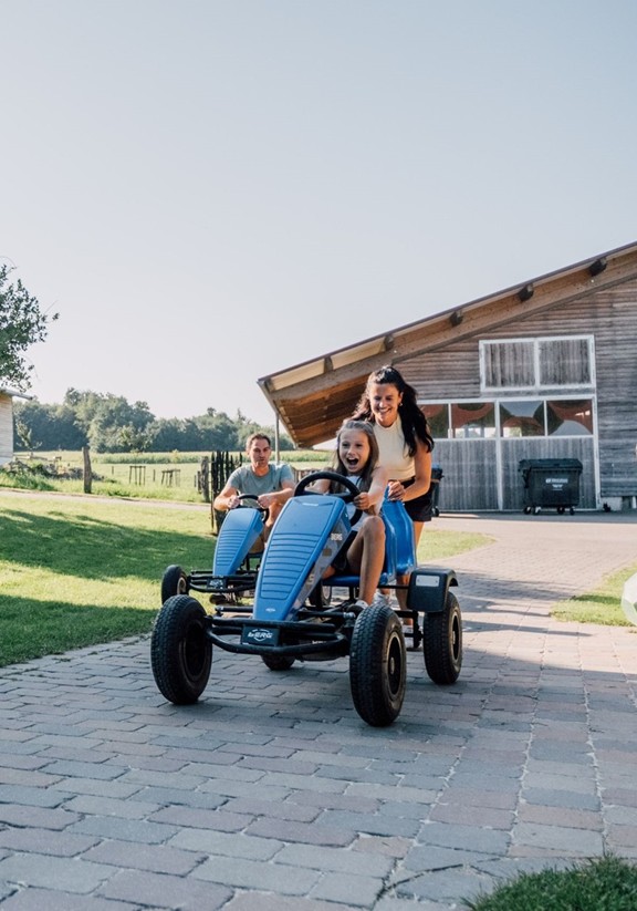Ein Kind fährt mit einem Tret-Traktor, eine Frau schiebt ihn von hinten an.