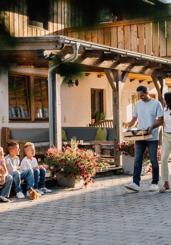 Ein Mann geht mit der Frühstücksbox, eine Frau hängt ihm am Arm, vor dem Haus sitzen drei Kinder und schauen die beiden an.